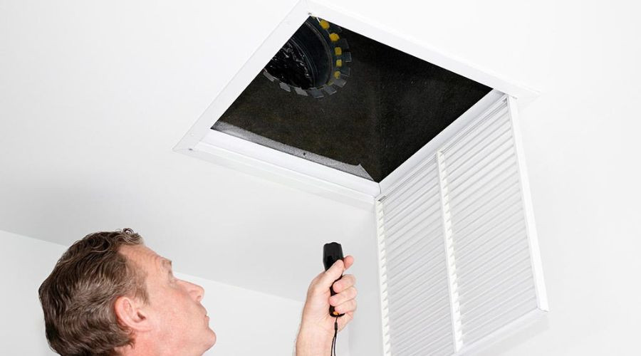 Man inspecting removable ceiling panel with flashlight for HVAC system maintenance by AirLux Heating & Cooling.